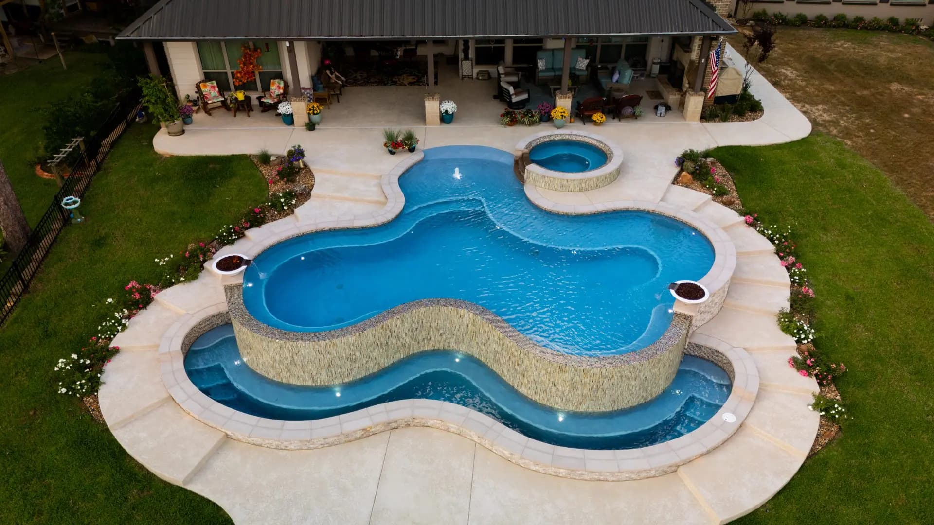 Aerial view of a custom freeform pool with a raised infinity edge, a spa and a covered patio
