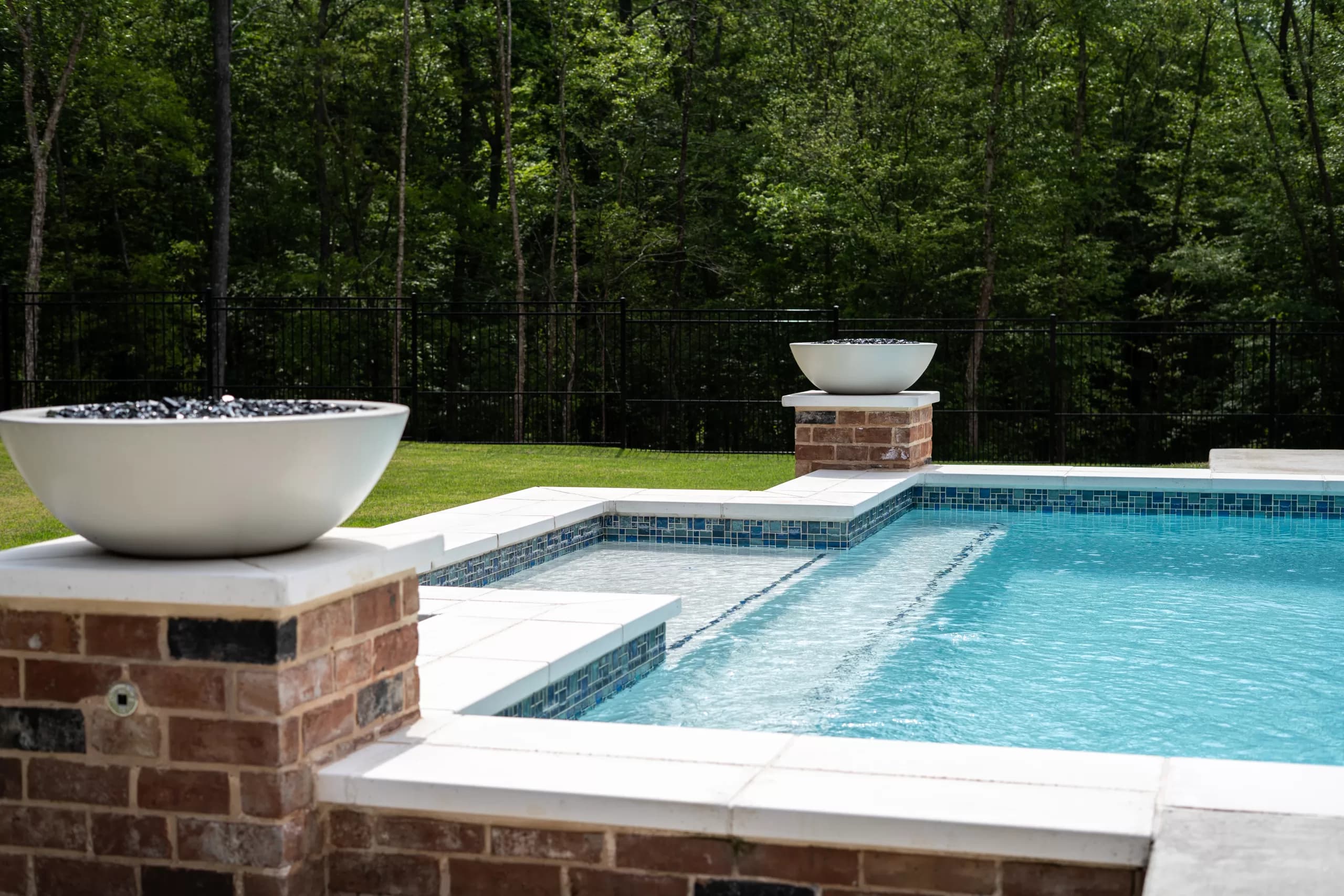 Custom pool with natural stone coping, a white fire bowl and a glass tile waterline