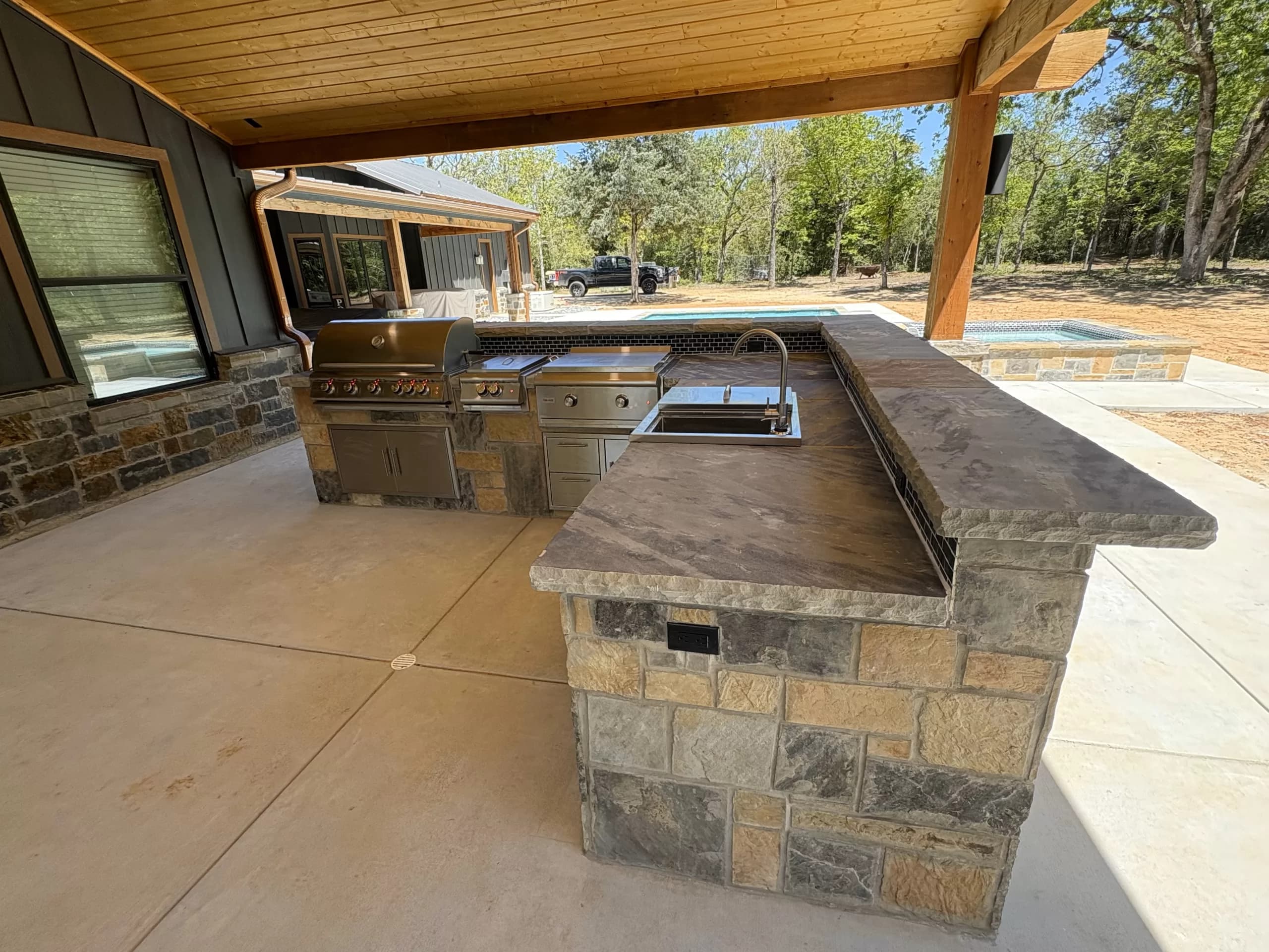 Outdoor kitchen with a stone bar and grill on a patio beside a pool