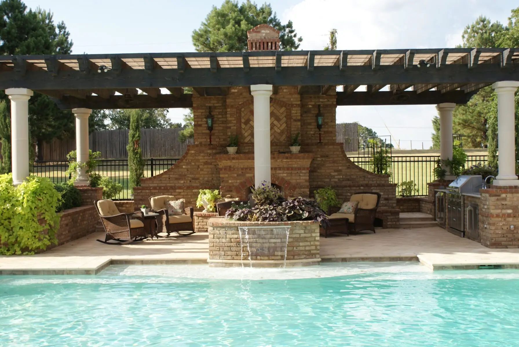 Brick outdoor fireplace under a pergola beside a pool